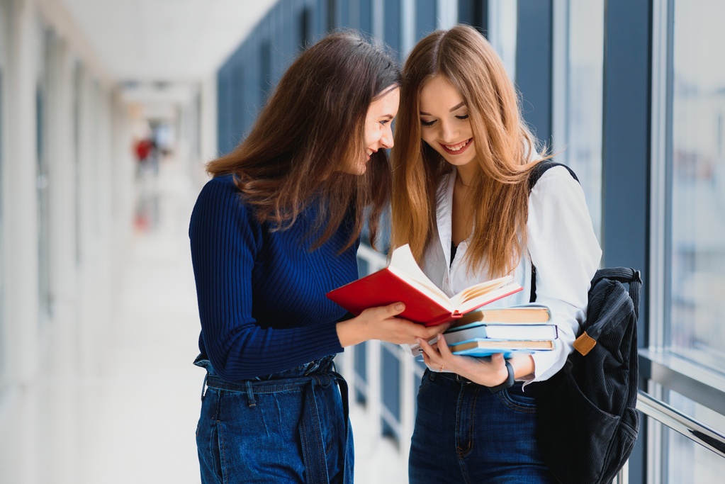 two-young-female-students-standing-with-books-bags-hallway.jpg