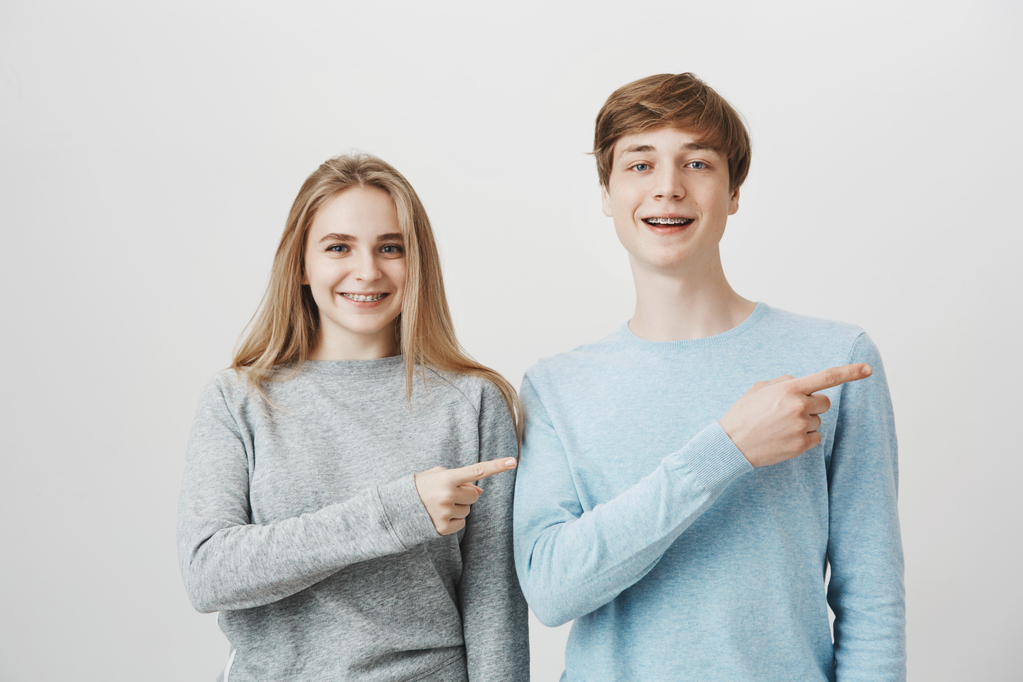 smiling-blond-guy-girl-with-braces-showing-way-pointing-fingers-right.jpg